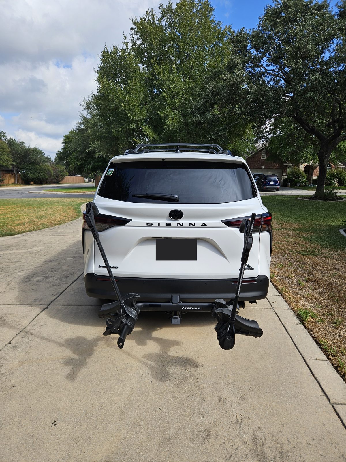 A K&uuml;at hitch bike rack mounted on the receiver of a white Toyota Sienna in a driveway, with no bikes loaded
