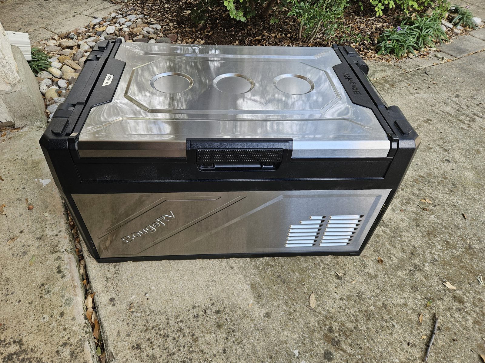 A BougeRV stainless and black 12 V compressor fridge standing closed on a driveway
