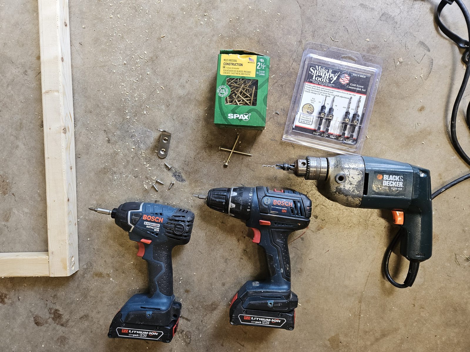 Three drills laid out on the bench with a pilot/countersink bit, a Torx driver and a Philips driver, beside a box of SPAX screws