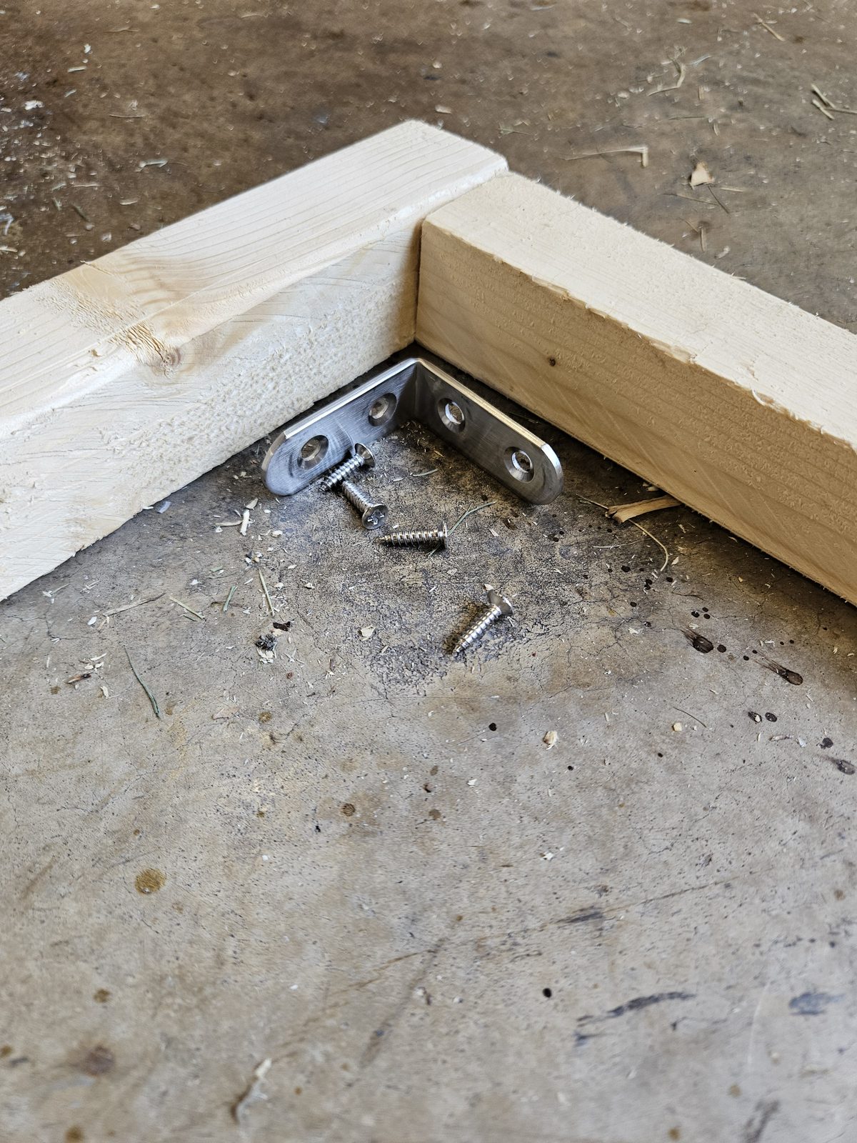 A flat steel corner bracket positioned inside a frame corner with its screws