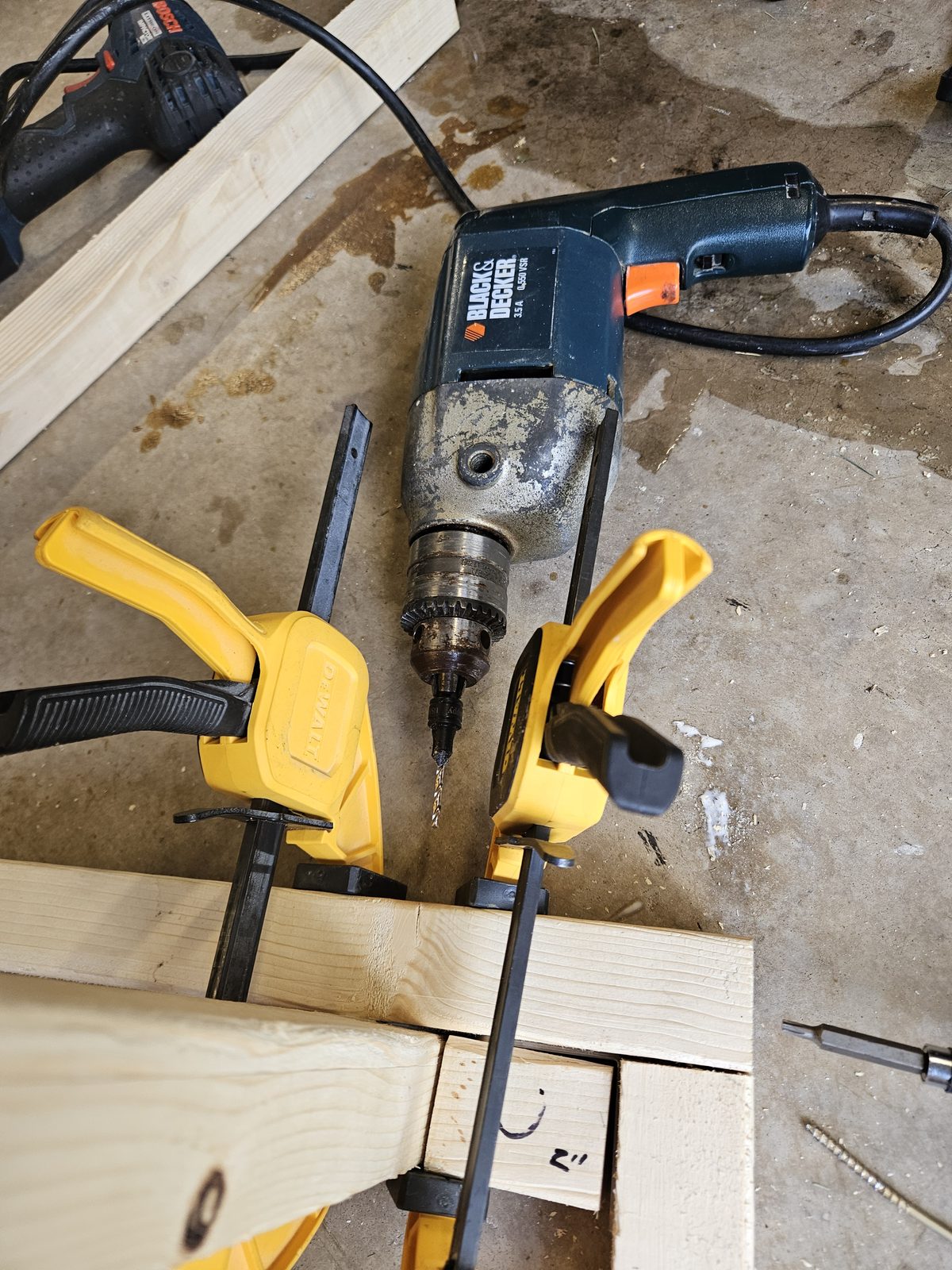 A leg clamped to the rail with two bar clamps, beside an offcut block marked 2 inches used as a setback gauge
