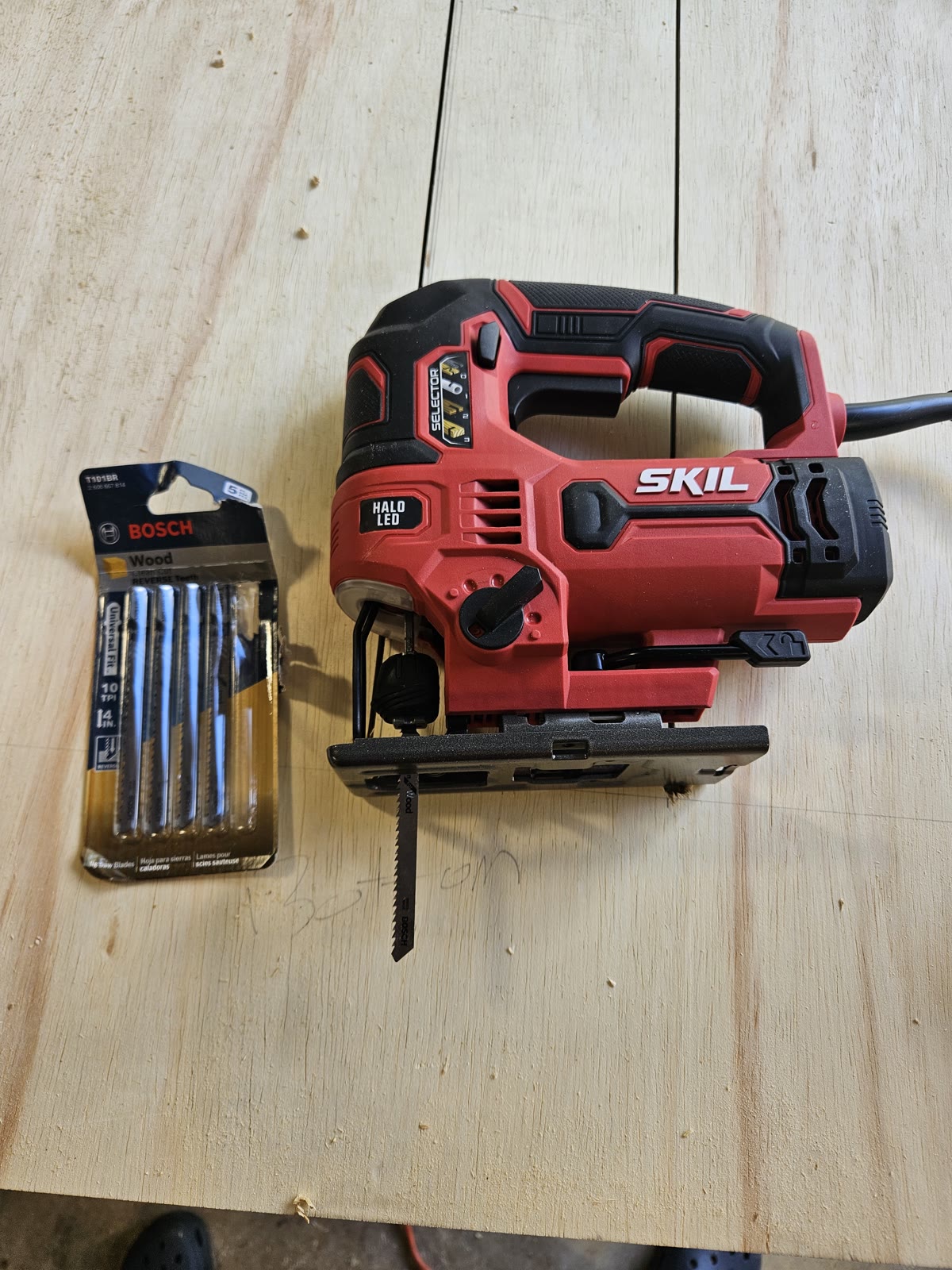 A SKIL jigsaw beside a pack of Bosch T101BR reverse-tooth wood blades on a plywood surface