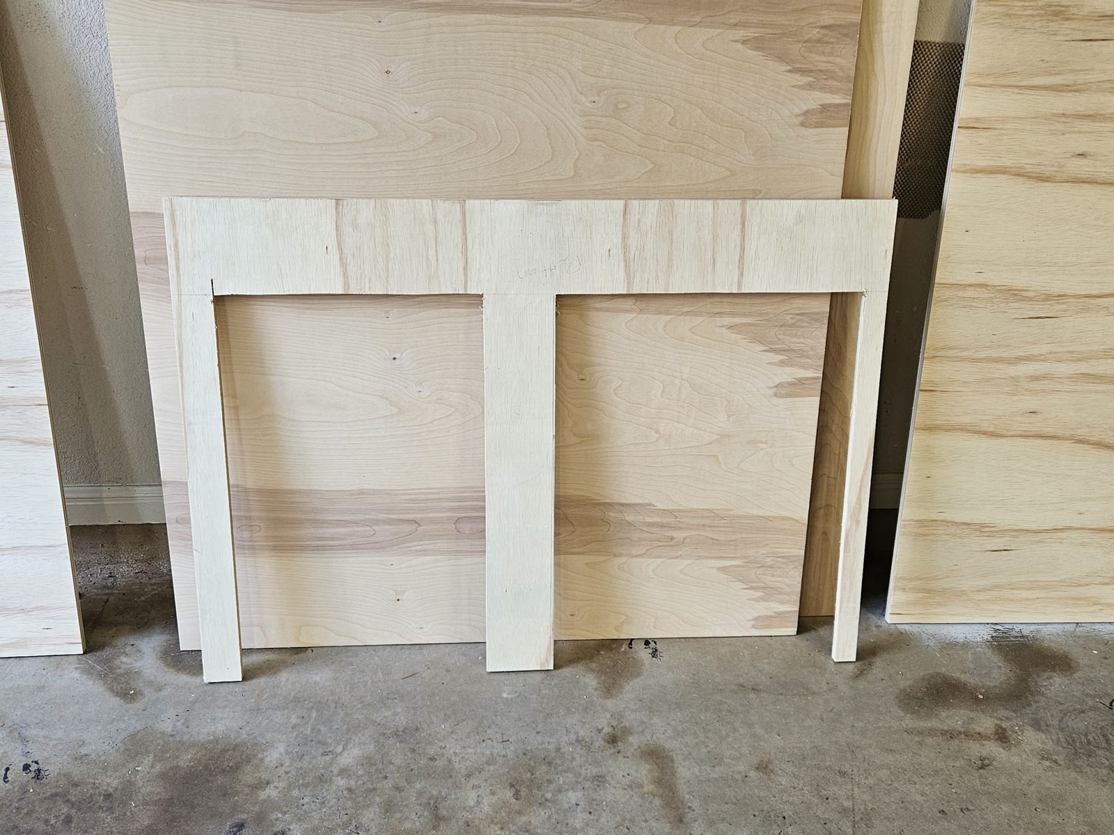 The finished one-piece plywood anchor board comb standing against a garage wall, showing a full-width bridge across the top with three strips running down from it