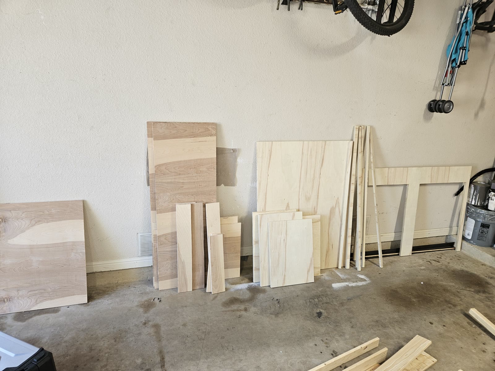 Every cut plywood part for the build stacked on edge against a garage wall, with the anchor board comb at right and ripped cleats alongside