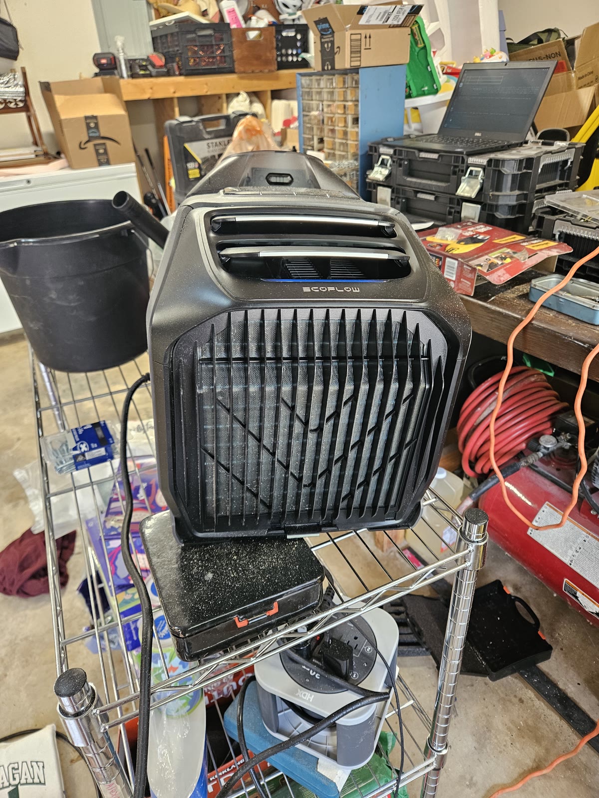 An EcoFlow WAVE 3 air conditioner running on a wire shelf in a garage workshop, stacked on its add-on battery